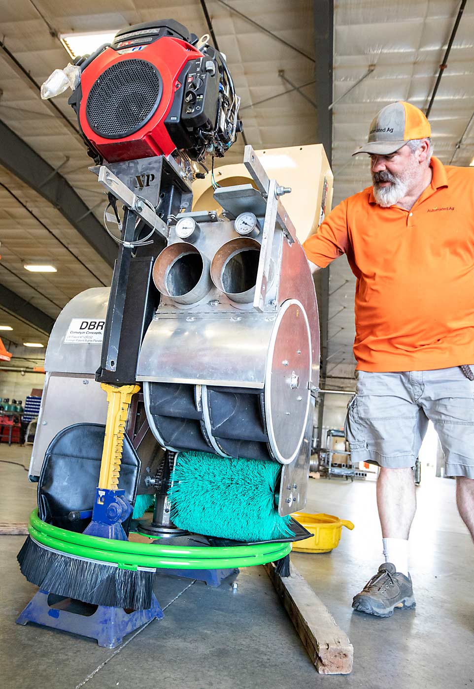 J.J. Dagorret muestra varios de los cambios que realizó en el prototipo de máquina de recolección por aspiración en Automated Ag Systems en junio. Lo único que queda de la versión original atornillada es el desacelerador en el centro de la máquina construido por DBR Conveyor Concepts. Desde arriba: el motor original de altas revoluciones por minuto se reemplazó por un motor más silencioso, las aspas y la carcasa del ventilador de extracción se rediseñaron para crear más succión, y el sistema óptico de transporte del contenedor fue reemplazado por un sistema de entrega mecánico preexistente desarrollado por MAF Industries. Dagorret dice que esta nueva versión fue rediseñada con base en los comentarios de los productores. (TJ Mullinax/Good Fruit Grower)