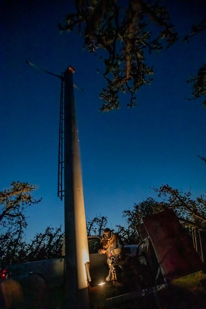 Aunque ahora las máquinas de viento se ponen en marcha automáticamente al bajar las temperaturas, el agricultor Connor Duim, de Cherry Ridge Orchards, en el valle de Yakima, Washington, sigue dependiendo de las previsiones de heladas para preparar su equipo y "asegurarse de que todo está listo para la noche", dice. En el abril del año 2021, Duim y su padre tuvieron que solucionar el problema de un conducto de combustible pinchado en esta máquina. (TJ Mullinax/Good Fruit Grower)