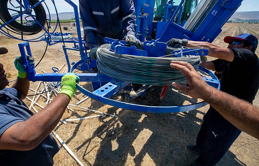 Durante una plantación comercial, los rollos de alambre, la tubería y los postes se transportan en un remolque detrás de la máquina, junto con las vides, para poder recargar en la mitad de una hilera, pero en la pequeña plantación de investigación de la WSU, el reabastecimiento tuvo lugar en el borde del viñedo, dando la oportunidad de ver bien cómo funciona la máquina a los asistentes al día de campo. (TJ Mullinax/Good Fruit Grower)