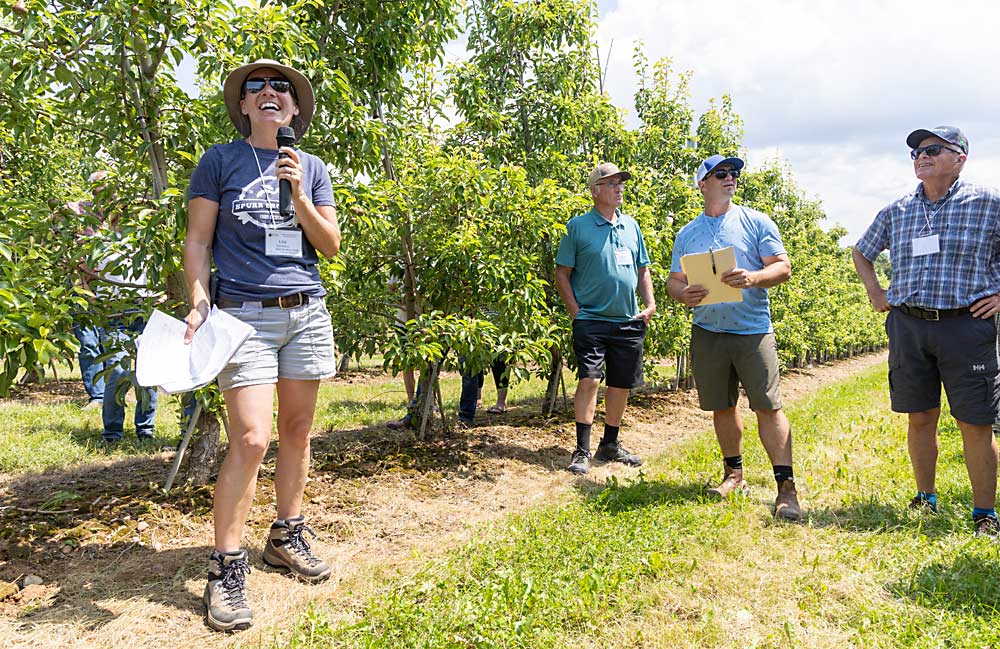 Lisa Jenereaux, a la izquierda, habla de los perales de su huerto con la Asociación Internacional de Árboles Frutales durante su visita a Nueva Escocia, Canadá en el mes de julio. Los árboles se plantaron con espaldera de forma en V para controlar el vigor y facilitar su manejo. (Matt Milkovich/Good Fruit Grower)
