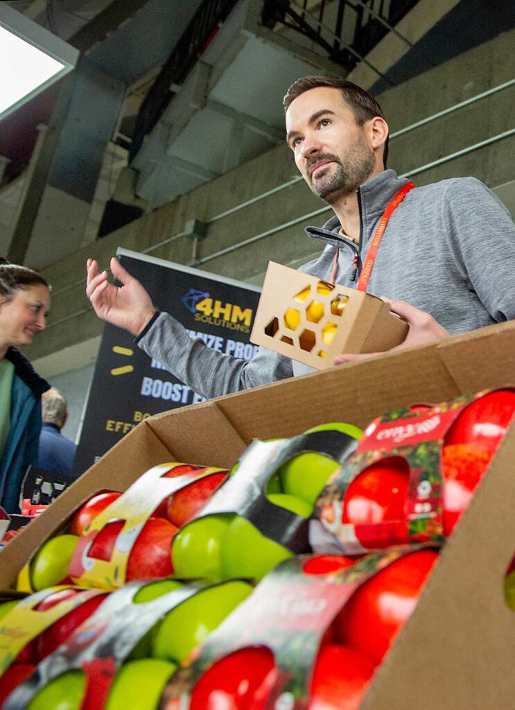 En diciembre del año pasado, Brant Carman, director de ventas para la costa oeste de EEUU de la compañía 4HM Solutions, presentó la maquinaria de su empresa que automatiza las cajas de cartón, en la reunión anual de la Asociación de Árboles Frutales del Estado de Washington (Washington State Tree Fruit Association) y la Exposición de Horticultura del Noroeste (2023 NW Hort Expo) de Kennewick. (Ross Courtney/Good Fruit Grower)