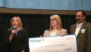 Jennifer Witherbee of the Washington Apple Education Foundation, left, thanks Walmart officials Shelly Palmer, holding a $25,000 mock check, and Michael Rainey during the Northwest Cherry Institute meeting in Yakima, Washington.