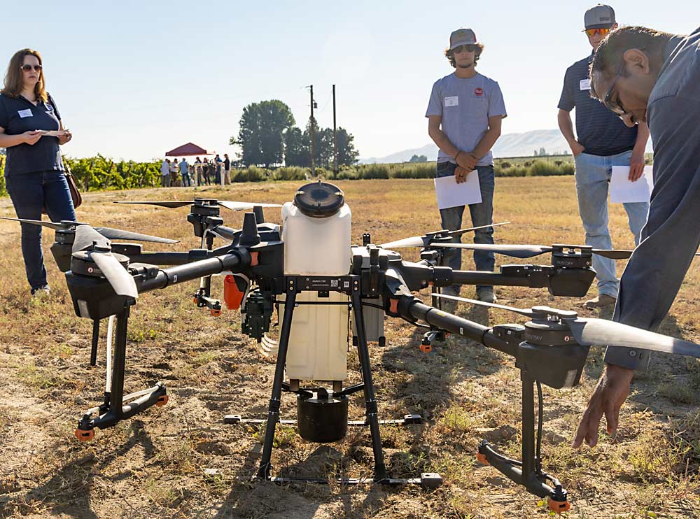 WSU associate professor Lav Khot, at right, explains how the drone uses standard spray nozzles — easily replaceable — and the downward blast of the rotors to generate its spray coverage. The modular design means the 20-liter spray tank and battery can be easily swapped in and out to extend the application time beyond the 12-minute flight time and 1 acre of coverage each battery offers. (Kate Prengaman/Good Fruit Grower)