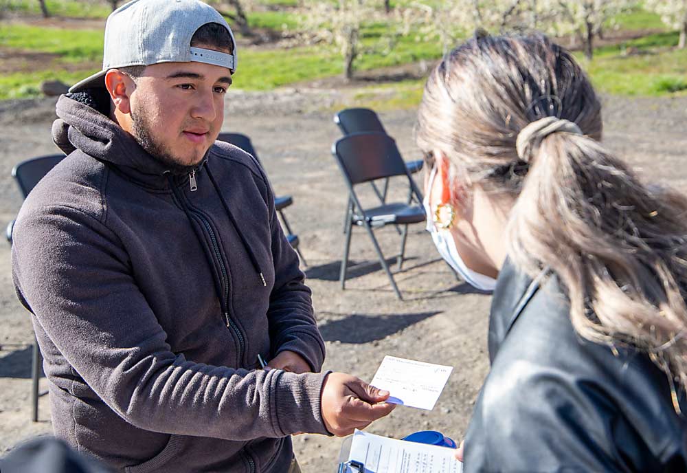 Farmworker Juan Carlos Cruz Mendoza of Michoacan, Mexico, shows his vaccination card to Laura De la Torre, outreach community health worker lead, in preparation for his COVID-19 booster from La Clinica, an RV operated by One Community Health, an Oregon nonprofit organization that serves the Columbia Gorge region. (Ross Courtney/Good Fruit Grower)
