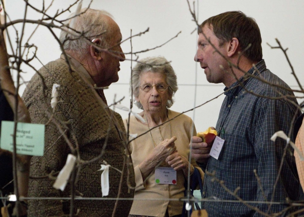 An Expo exhibit showing how to prune and train tall spindle apple trees, using various styles of clips, drew grower interest during the three-day show, December 10-12, 2013. Here, 85-year-old Bastian Blok and his wife, Ann, talk to Mike Rasch, one of the designers of the DBR vacuum harvester. (TJ Mullinax/Good Fruit Grower)