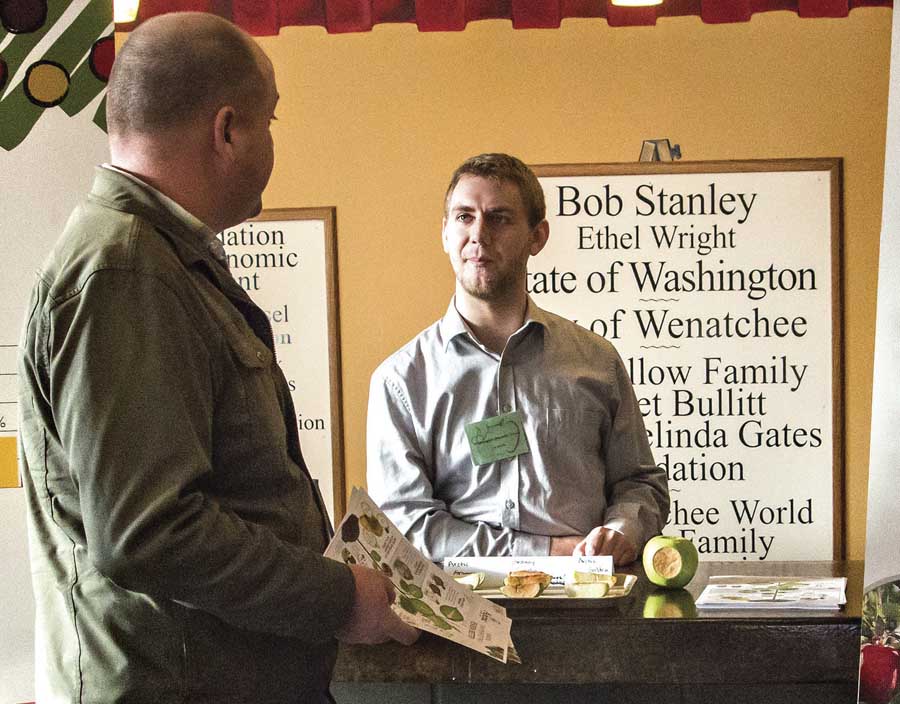 Arctic Apple employee, Joel Brooks, right, talks with an attendee of the Washington State Horticultural Association show on December 4, 2013 in Wenatchee, Washington. (TJ Mullinax/Good Fruit Grower)