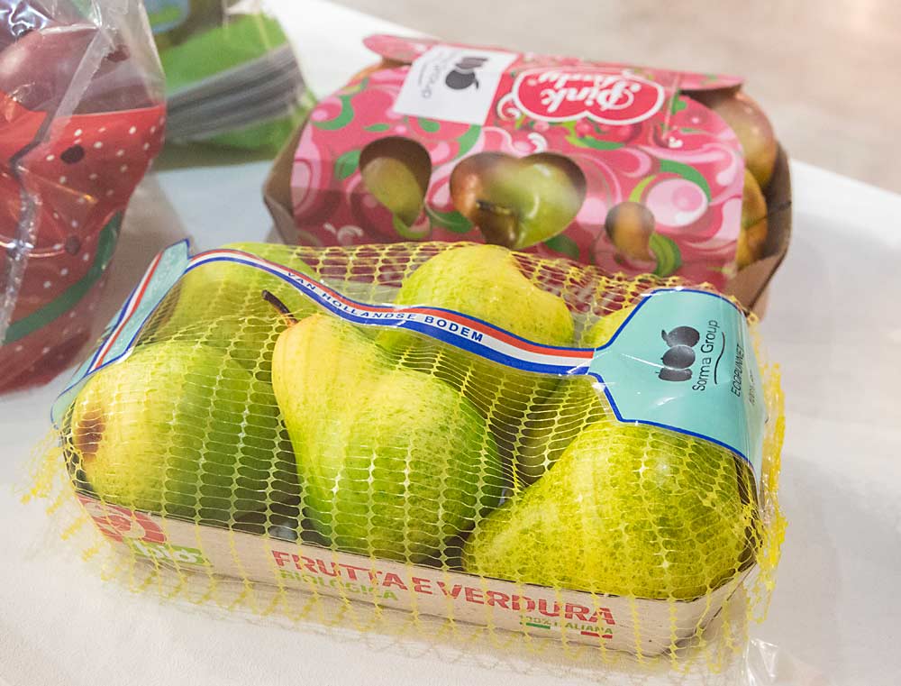 Sustainable packaging, such as this biodegradable webbing over pears and the cardboard apple box behind it, was a common theme on the Interpoma trade show floor. (Ross Courtney/Good Fruit Grower)