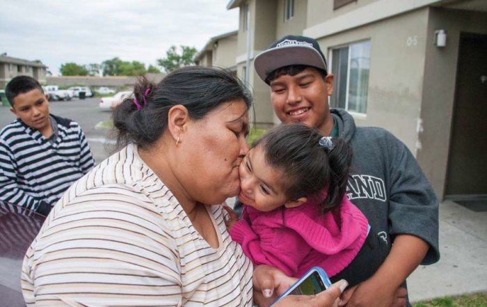 Beatriz Lara bids farewell to her granddaughter Ana Robledo outside Lara’s apartment at the Orchard Homes farmworker housing facility in Milton-Freewater, Oregon, in May. Holding Robledo is Lara’s son Javier Lara. The family lives at the complex year-round while working in nearby orchards. The farmers who own the building would like to use it to house visiting H-2A workers, but their U.S. Department of Agriculture loan requirements restrict the facility to U.S. citizens and permanent residents. (Ross Courtney/Good Fruit Grower)