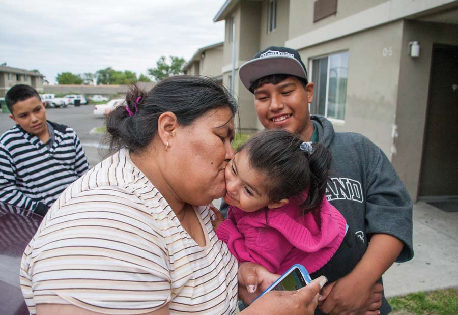 Beatriz Lara bids farewell to her granddaughter Ana Robledo outside Lara’s apartment at the Orchard Homes farmworker housing facility in Milton-Freewater, Oregon, in May. Holding Robledo is Lara’s son Javier Lara. The family lives at the complex year-round while working in nearby orchards. The farmers who own the building would like to use it to house visiting H-2A workers, but their U.S. Department of Agriculture loan requirements restrict the facility to U.S. citizens and permanent residents. (Ross Courtney/Good Fruit Grower)