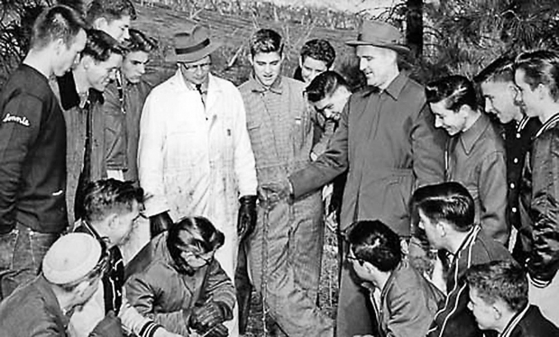 Dick Bartram (wearing the dark coat and hat) was an authority on orchard economics. Here, he explains how to get new trees off to a good start. Washington State University