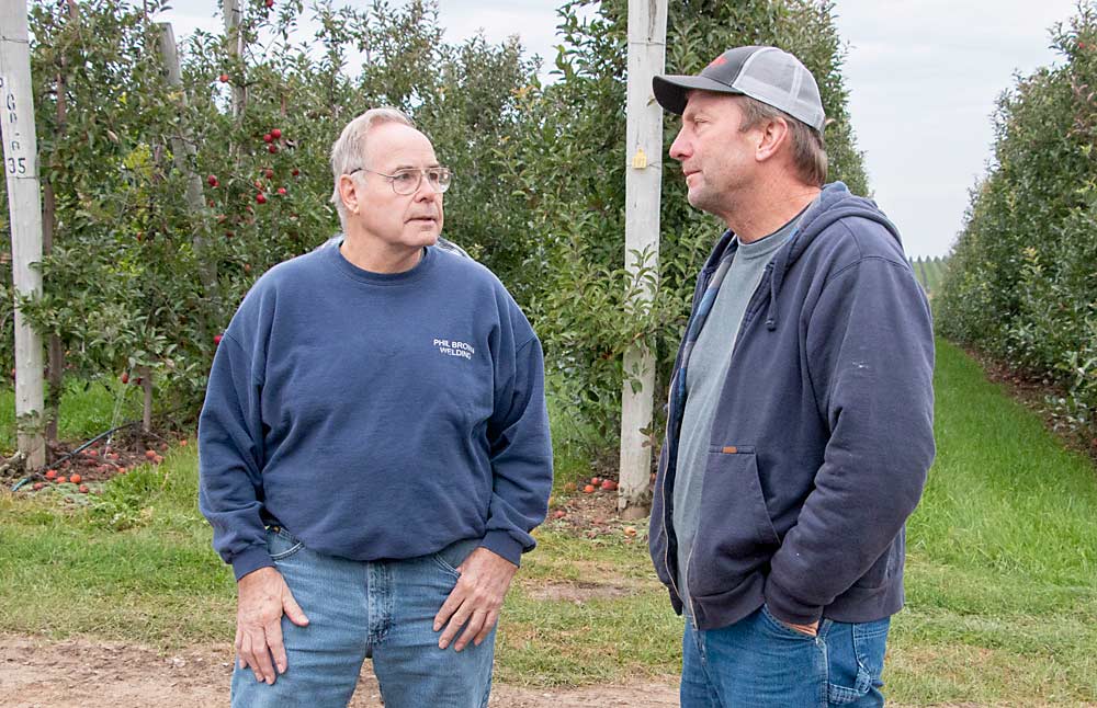 Phil Brown, left, and Mike Rasch, the “B” and “R” in DBR Conveyor Concepts, observe the 2019 version of their apple vacuum harvester at a Riveridge Produce Marketing orchard in Sparta, Michigan, last fall. DBR teamed up with Automated Ag Systems in Washington state to improve the machine. (Matt Milkovich/Good Fruit Grower)