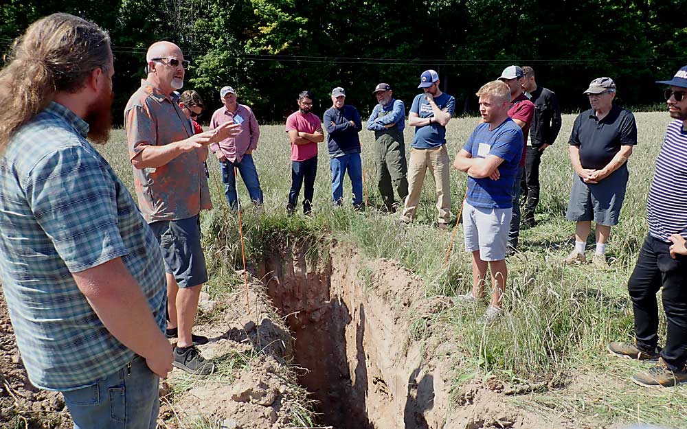 The soil pit at Rosi Vineyard in Traverse City, Michigan, showed more moisture retention than pits at other sites on the “Dirt to Glass” tour hosted by Michigan State University Extension in August. Vineyard soil researcher Kevin Pogue (second from left, in sunglasses) noted that soil moisture depth is just one of many characteristics revealed by a visual examination of soil at depths of several feet. (Leslie Mertz/for Good Fruit Grower)