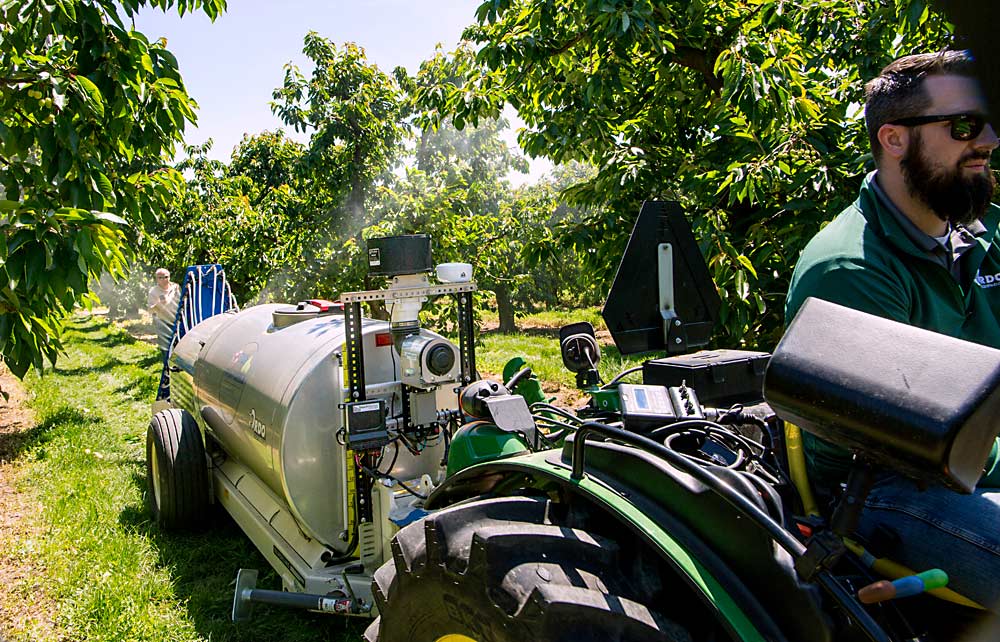 Dustin Heyen, a sales representative for RDO Equipment, demos a Blueline Accutech sprayer with a Smart Guided Systems intelligent control in May at Henry Bosma Orchards in Zillah, Washington. The control system only triggers valves to release spray when it senses foliage, shutting them off between trees. The system sprayed only water during the demo. (Ross Courtney/Good Fruit Grower)