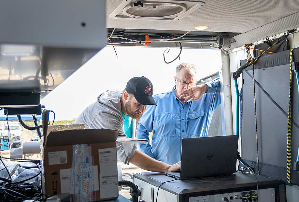 Collins, right, looks over real-time readings on specialized lab equipment measuring the volatile compounds present in the smoke being piped into the vineyard, with Matt Erickson, left, whose Pasco, Washington-based company, AtmosVITAL, loaned the proton-transfer-reaction mass spectrometer for the research project. (Kate Prengaman/Good Fruit Grower)