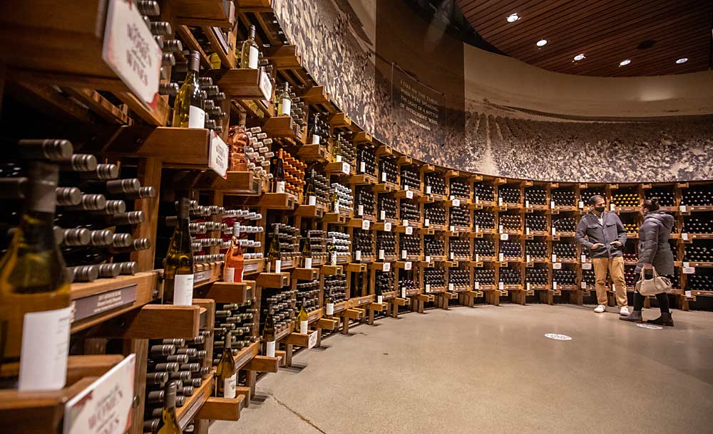 Customers shop in March 2021 next to a wall of wine in the Ste. Michelle Wine Estates tasting room in Woodinville, Washington. Ste. Michelle, which accounts for more than half of Washington’s wine shipments, has told growers it needs to reduce volume by 40 percent in the coming years, starting with some existing contracts. (TJ Mullinax/Good Fruit Grower)