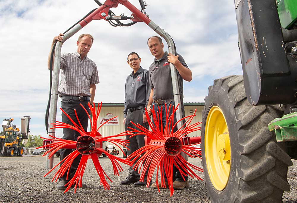 Manoj Karkee, center, a Washington State University associate professor of biological systems engineering, poses in mid-June with Jack Maljaars, left, and Grant De Vries of Vine Tech Equipment behind two mechanical shoot thinning cylinders, the automation of which is being commercialized through a partnership between WSU and Vine Tech. The collaboration is funded by the Washington State Wine Commission. (Ross Courtney/Good Fruit Grower)