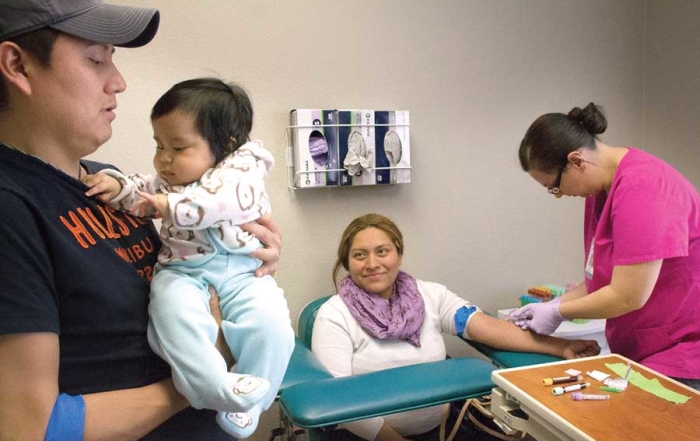 Stemilt Growers employee Alfonso Perez holds his 6-month-old daughter, Lexi Amaya, while wife Claudia Rea has blood drawn March 29, 2016, as part of her wellness exam at the Stemilt Family Clinic in Wenatchee, Washington. (Shannon Dininny/Good Fruit Grower)