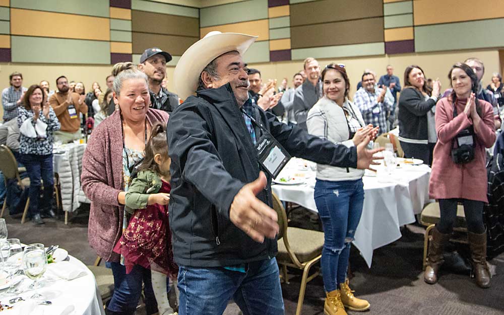Hipolito Vargas, the 40-year supervisor of Champoux Vineyards, reacts to being named the Grower of the Year on Feb. 9 in Kennewick, Washington, at WineVit, the state wine industry’s annual conference. His wife Martha, who helped bring his family to the awards luncheon to surprise him, looks on from behind. (Ross Courtney/Good Fruit Grower)