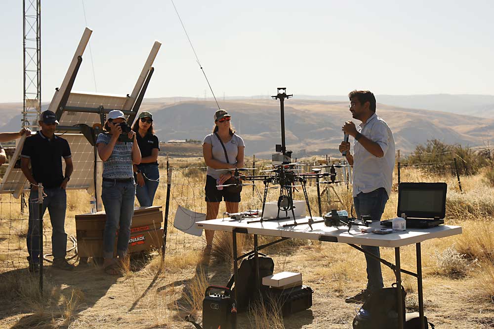 Srikanth Gorthi, right, a graduate student at WSU, discusses drone options he and his collaborators use to take accurate temperature measurements during inversions and other periods of frost risk.  The larger drone collects research data to build risk models, while the smaller drone next to it could prove to be a low-cost tool that growers could deploy to measure the behavior of cold air in their orchards.  (Kate Prengaman/Good Fruit Grower)