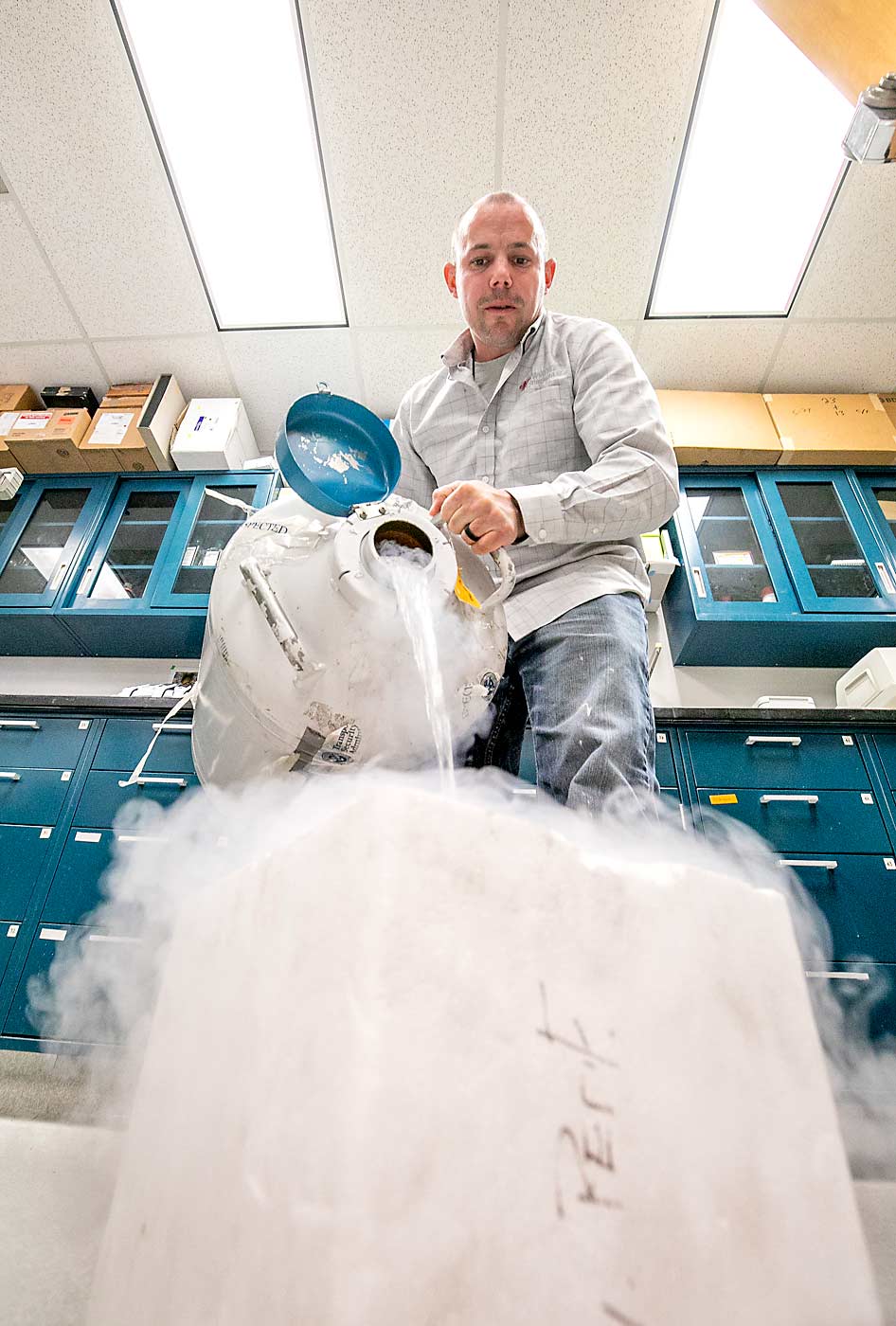 Brandon Hopkins pours liquid nitrogen over bee semen samples in a plastic foam container to keep them cold before selecting a single vial to thaw for insemination. (TJ Mullinax/Good Fruit Grower)