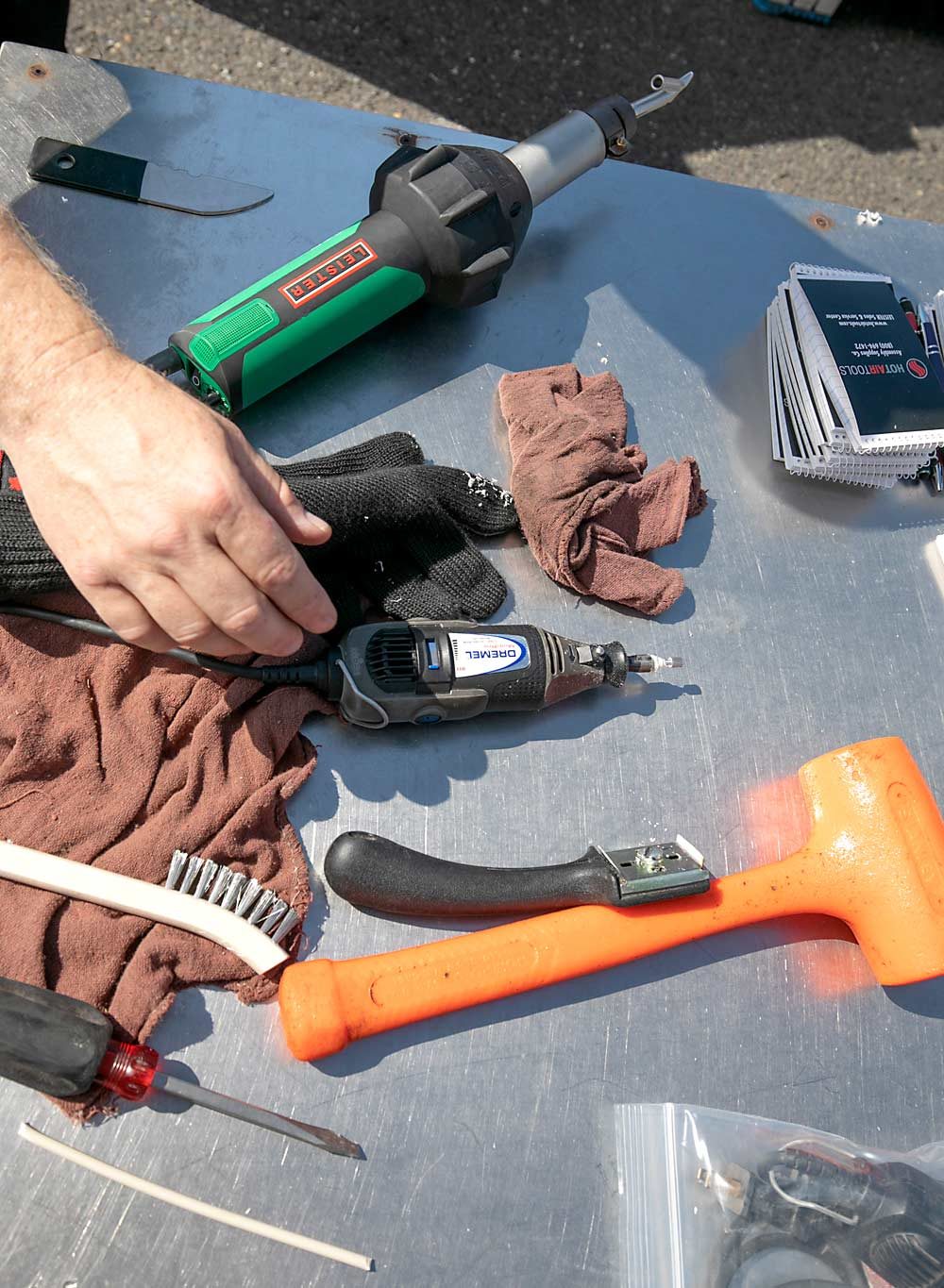 A few common tools and materials for plastic bin repairs, clockwise from top left: a blade, hot-air welding tool, grinder/Dremel, scraper blade, mallet, plastic welding rod, screwdriver and wire brush. (TJ Mullinax/Good Fruit Grower)