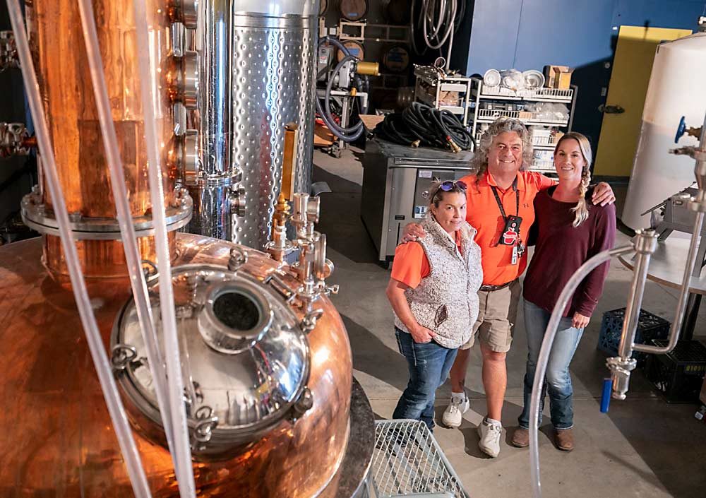 Craver poses with his daughters, Sarah Craver, left, and Janette Thompson, in a still owned by New Royal Bluff Orchards. The company, which uses culled fruit to make spirits, is ramping up its volume before marketing its wares. (TJ Mullinax/Good Fruit Grower)