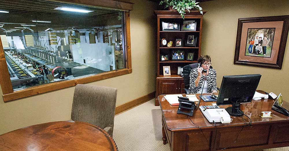 Jill Douglas in her office in 2014 as workers can be seen packing apricots behind her. She assumed the role of general manager at age 24 in 1989 and retired in 2020. (TJ Mullinax/Good Fruit Grower)
