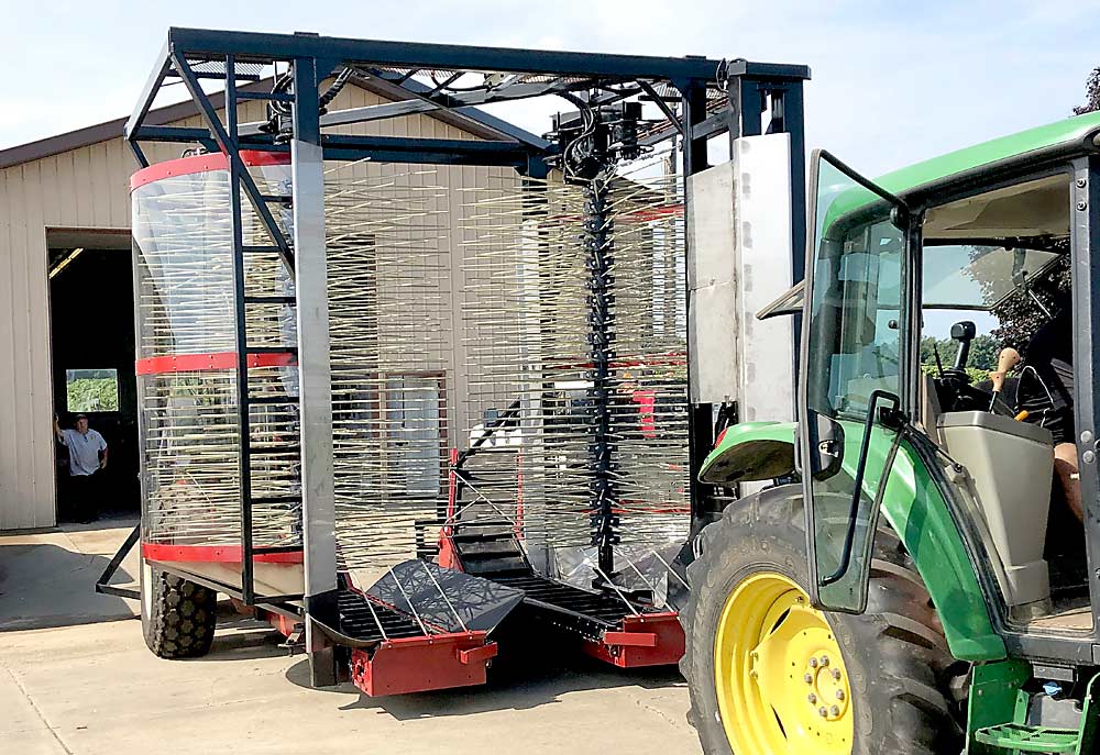 The harvester is pulled by a tractor and is powered by the tractor’s power take-off. The hydraulic hitch connecting the two machines swings in for road transport and out for picking, to keep the tractor out of the way of the trees. (Courtesy Oxley Farms)