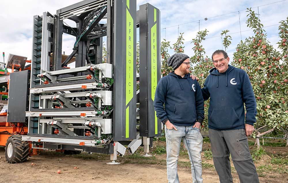 Kahani, right, and engineer Or Hilshfeld pose in front of FFRobotics’ protoype. Their next iteration will be smaller and lighter and allow a bin to pass through the machine, they said. (TJ Mullinax/Good Fruit Grower)
