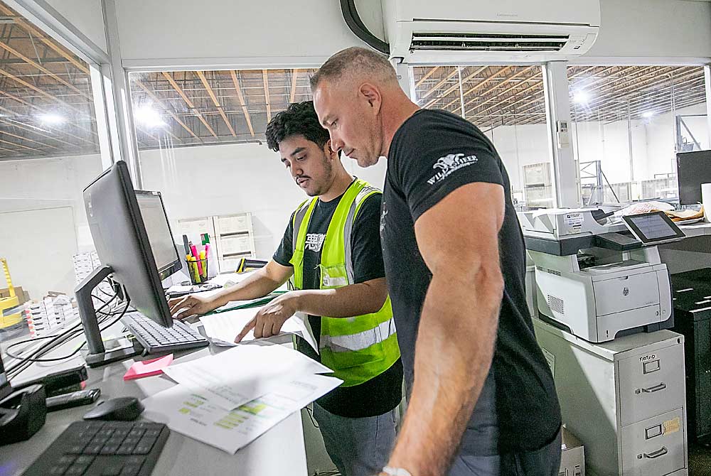 Pete Douglas, right, checks in with Eric Giron as organic peaches roll on the line below. The stone fruit program must manage many more SKUs than the apple program, Douglas said. (TJ Mullinax/Good Fruit Grower)