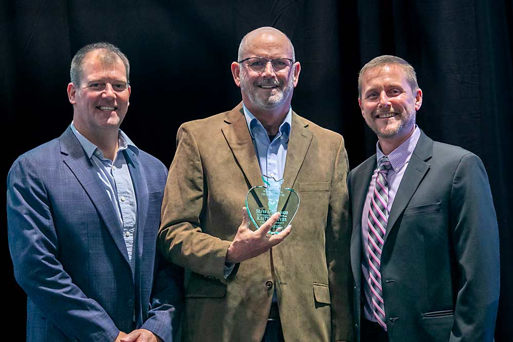 Known for hosting field days and sharing information, Keith Oliver, center, receives the Silver Apple Award presented by Mark Hambelton, left and Marty Olsen, right. (TJ Mullinax/Good Fruit Grower)