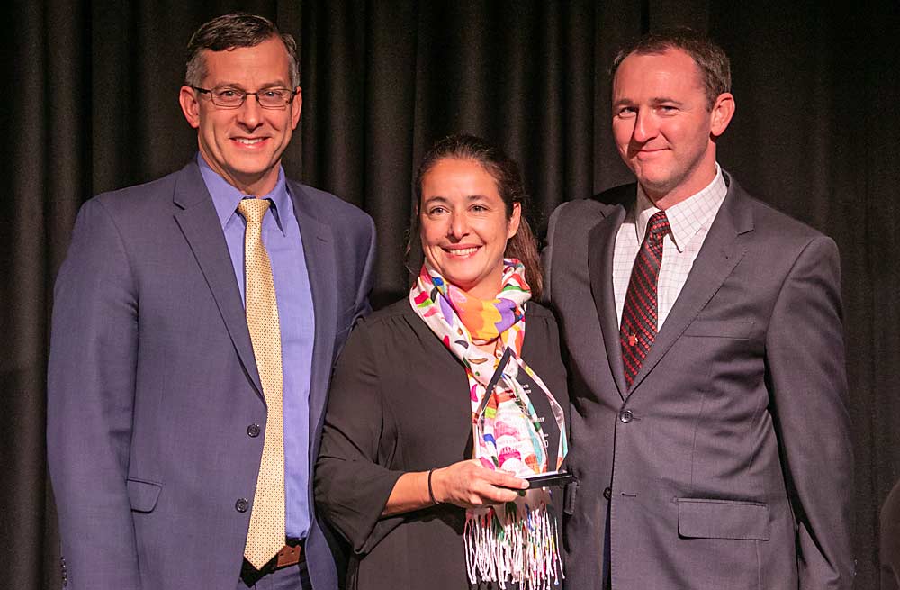 Jared England, left, and Jordan Matson, right, present the Latino Leadership Award to Bernardita Sallato during the 2022 Washington State Tree Fruit Association Annual Meeting on Dec. 6 in Wenatchee, Washington. (TJ Mullinax/Good Fruit Grower)