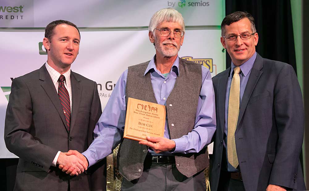 Jordan Matson, left, and Jared England, right, present the Distinguished Service Award to Bob Gix during the Washington State Tree Fruit Association Annual Meeting on Tuesday, Dec. 6, 2022, in Wenatchee, Washington. (TJ Mullinax/Good Fruit Grower)