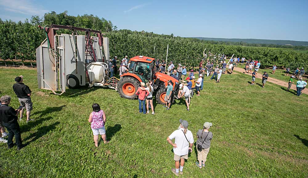At CAP Farms, the International Fruit Tree Association summer tour group saw a homemade over-the-row sprayer, as well as a block of high-density Ambrosia, left, and top-worked Honeycrisp, right. IFTA held its 2023 summer tour in Nova Scotia, Canada, in July. (TJ Mullinax/Good Fruit Grower)