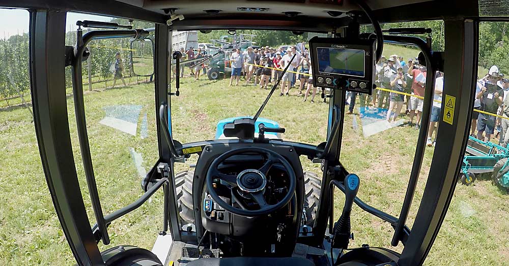 A photo taken from inside the cab of a New Holland tractor equipped with a GOtrack autonomy kit as IFTA members watch the tractor drive itself through an apple block at Van Meekeren Farms in Centerville. (TJ Mullinax/Good Fruit Grower)