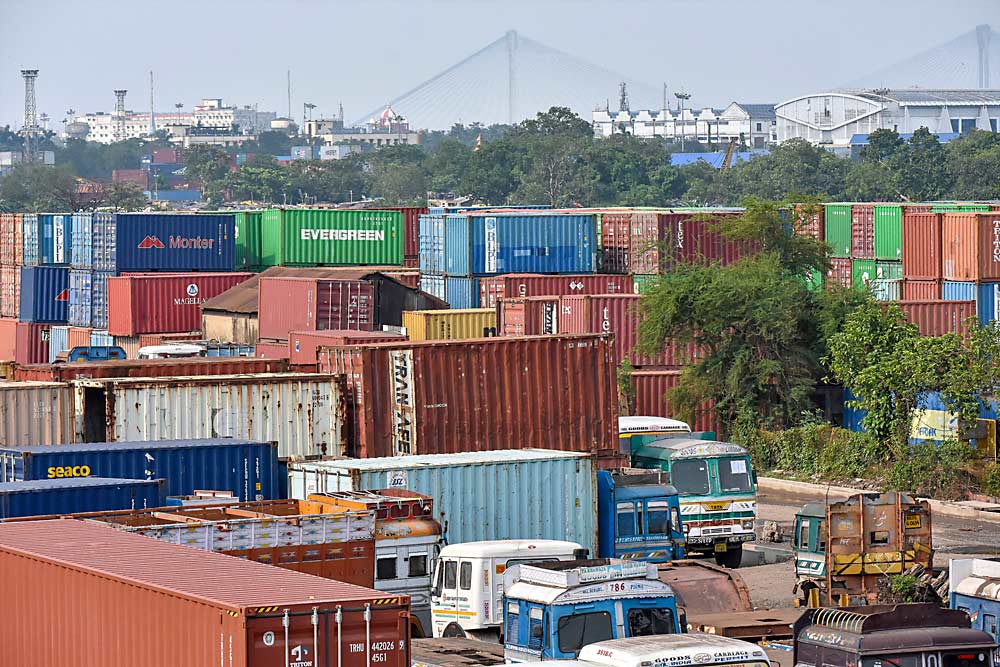 Containers are stacked at the Syama Prasad Mookerjee Port in May in Kolkata, India, while the Vidyasagar Setu bridge towers in the distance. Pandemic-related supply chain snarls, as well as lingering high tariffs, have reduced America’s apple exports to India to a fraction of their volumes just a few years ago. (Debarchan Chatterjee/The Associated Press)