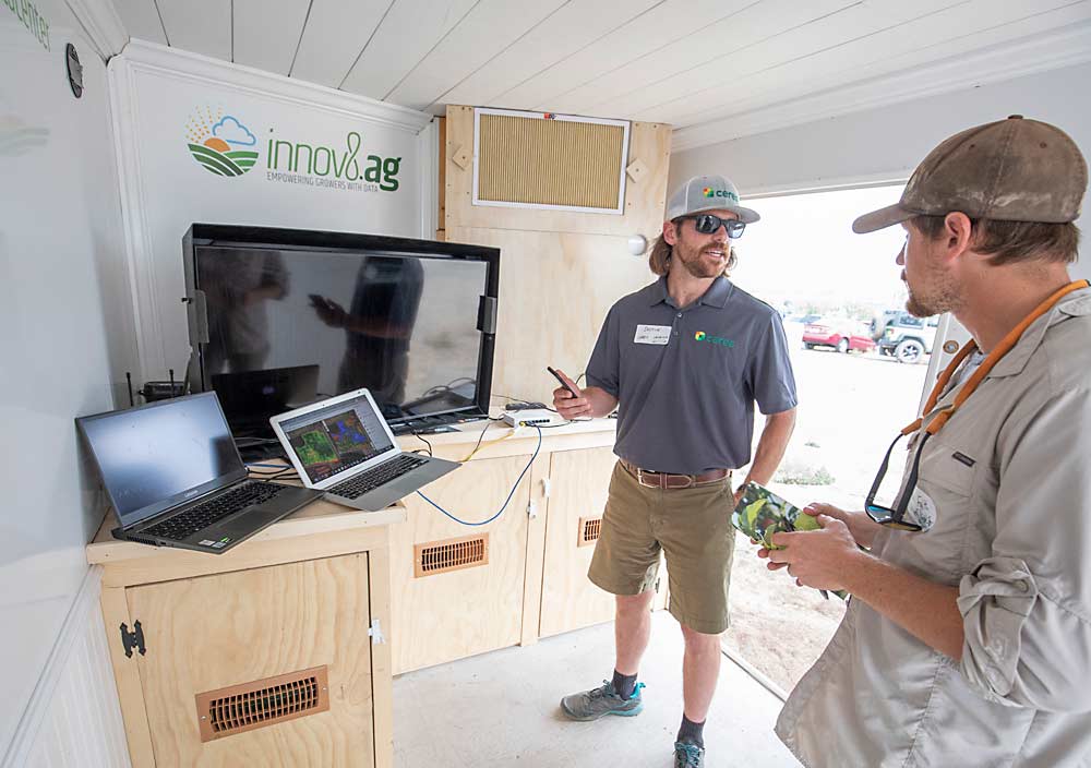 Ceres Imaging representative Dustin Gargas, left, talks with a field day attendee inside innov8.ag’s mobile data center. Mantle designed the data center — a trailer outfitted with servers and a generator — to process the enormous volume of data developed by imaging sensors on site. (TJ Mullinax/Good Fruit Grower)