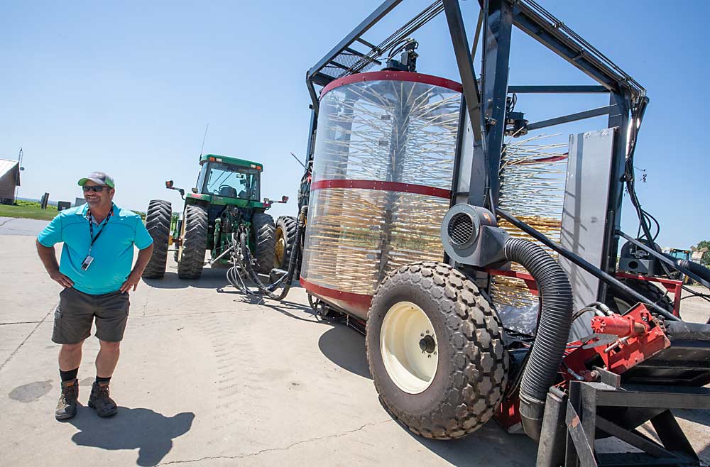 Chris Oxley next to his family’s over-the-row tart cherry harvester, which they designed and built themselves. The machine’s many tines shake young cherry canopies the same way a blueberry harvester shakes blueberry bushes. (TJ Mullinax/Good Fruit Grower)