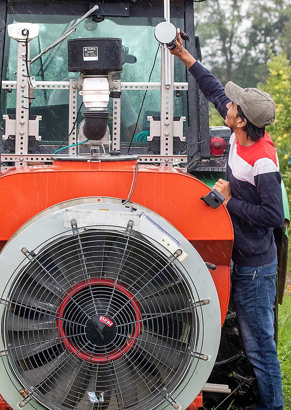 Penn State graduate research assistant Md Sultan Mahmud adjusts the lidar sensor attached to the experimental airblast sprayer at the Biglerville research orchard. The sensor was originally attached to an ATV, but the team eventually attached it directly to the sprayer. (TJ Mullinax/Good Fruit Grower)