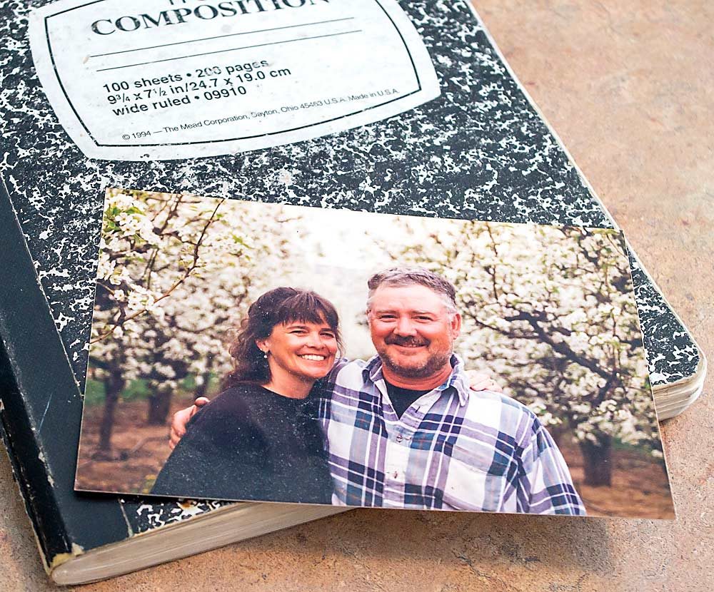 Smith’s favorite photograph of her husband rests atop one of the farm journals Steve Smith kept. In the photograph, the Smiths are standing in their pear orchard, and she is wearing her signature pearl earrings. “People would always say, ‘She farms in pearls?’” Smith said. (Jonelle Mejica/Good Fruit Grower)